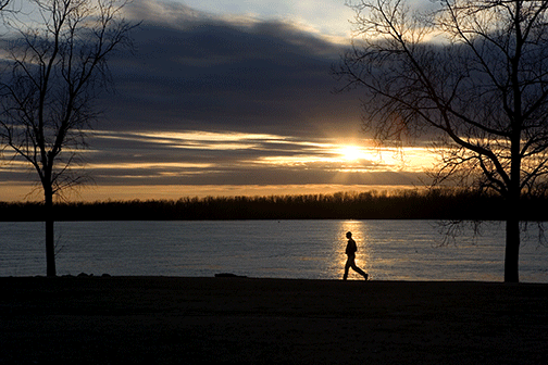 Man jogging caught in setting sun against river